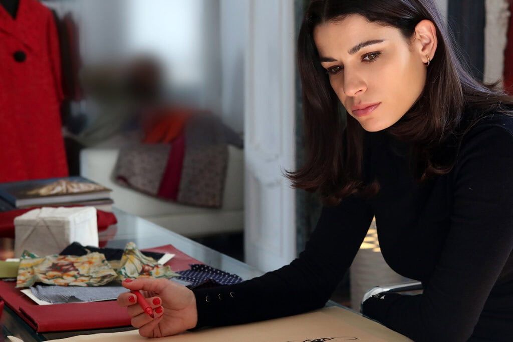 Mujer diseñando moda en estudio con telas y bocetos.