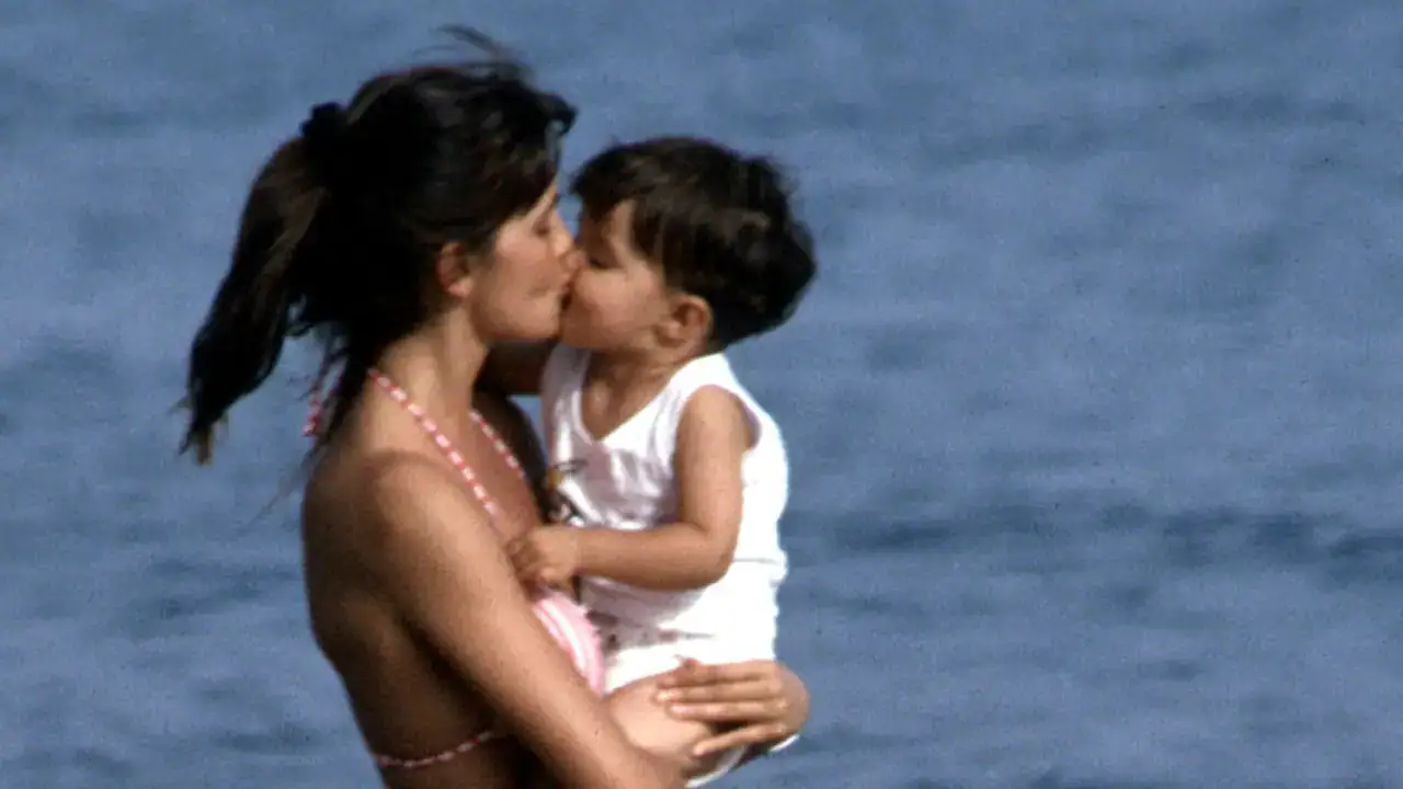 Madre e hija compartiendo un beso en la playa, simbolizando amor y unión familiar.