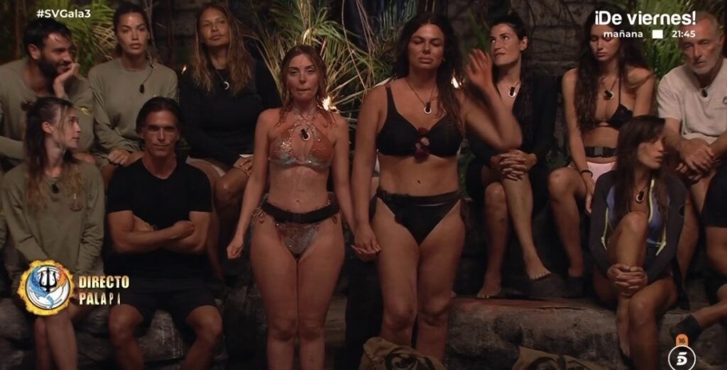 Dos concursantes permanecen de pie ante sus compañeros sentados en la palapa de Supervivientes 2026 durante la gala en directo