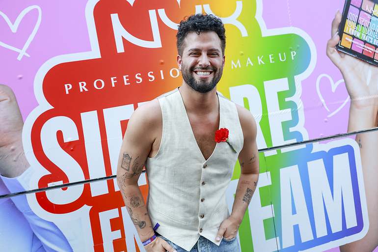 Javi de Hoyos sonríe con chaleco de lino y un clavel rojo ante un photocall arcoíris del Orgullo